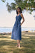 Woman wearing a blue medium wash denim A-line sleeveless dress with belt and frayed midi hem from Joseph Ribkoff