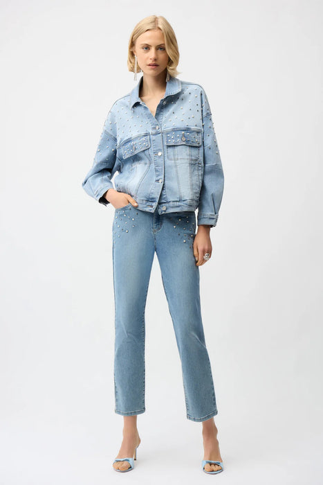 Woman wearing Joseph Ribkoff denim oversized jacket with pearls and studs, featuring embellished light-wash denim, relaxed fit, classic collar, and statement detailing.