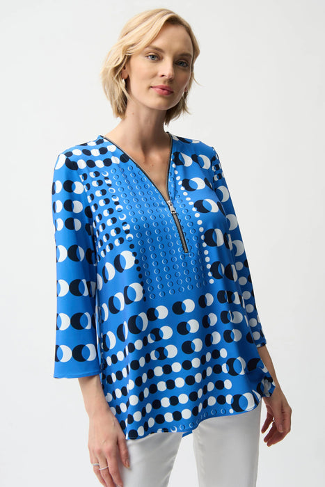 Woman wearing Joseph Ribkoff dot print fit and flare tunic with zipper, featuring a bold blue pattern, flowy silhouette, and stylish three-quarter sleeves.