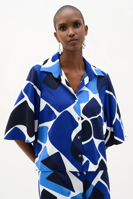 Woman wearing Joseph Ribkoff blue and white geometric print straight blouse, featuring a bold patterned design, relaxed silhouette, lightweight fabric, and a polished modern fit.