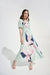 Woman wearing a green pleated satin maxi dress with bold floral patterns and waist tie from Joseph Ribkoff