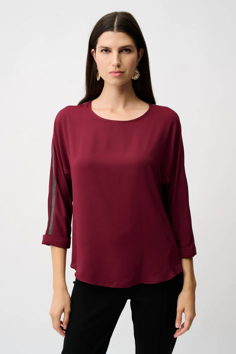Woman wearing a burgundy lightweight blouse with contrasting rhinestone embellishments on the 3/4 sleeves
