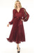 Woman wearing a red pleated satin fit and flare midi dress with wrap neckline, lace insert on the puff sleeves, and waist sash from Joseph Ribkoff