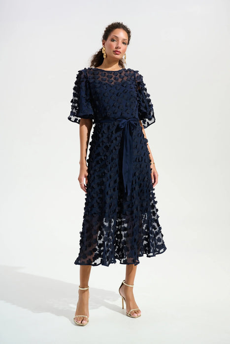 Woman wearing a dark blue midi dress with 3D floral details and waist sash from Joseph Ribkoff