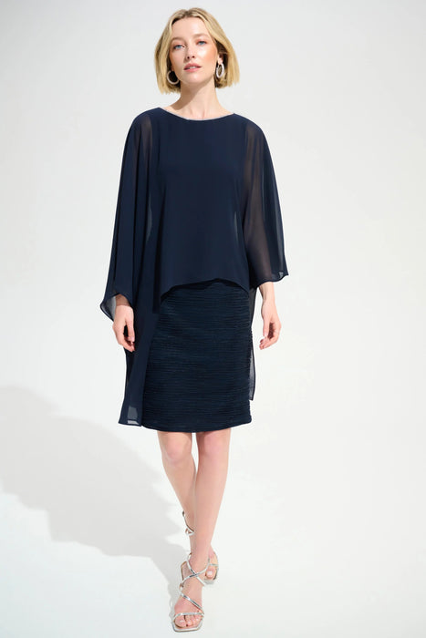 Woman wearing a dark blue textured sheath dress with lightweight chiffon poncho overlay from Joseph Ribkoff