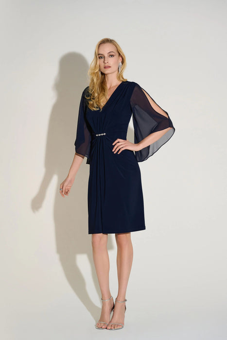 Woman wearing a dark blue sheath dress with ruching at the front and sheer chiffon slit sleeves