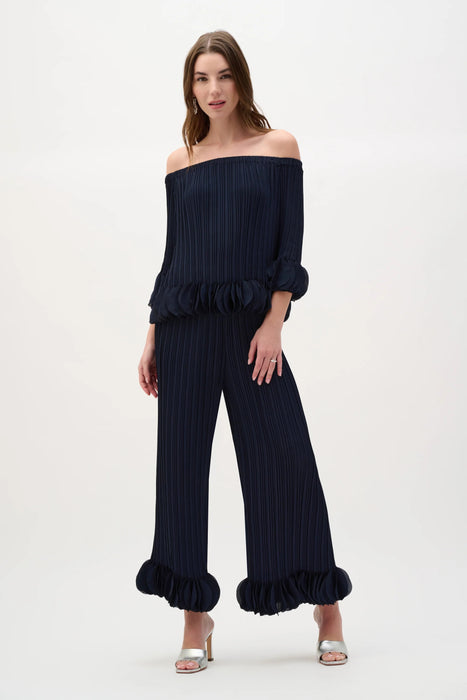 Woman wearing a Joseph Ribkoff georgette off-shoulder pleated top with cascading ruffle sleeves and sculptural peplum detail at an elegant evening event.