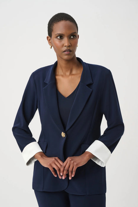Woman wearing a dark blue fitted blazer jacket with flap pockets and gold rose button from Joseph Ribkoff