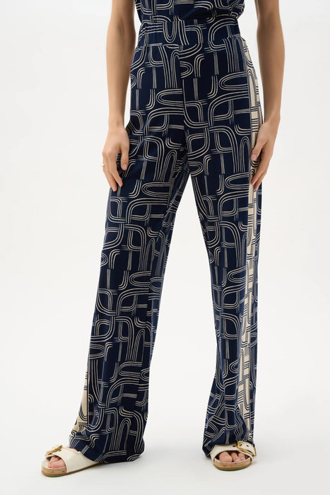 Woman wearing Joseph Ribkoff geometric print wide leg pull-on pants, featuring a bold modern pattern, flowy silhouette, elastic waistband, and a flattering elongated fit.