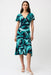 Woman wearing a green and black abstract strokes patterned dress with ruffled midi hem from Joseph Ribkoff