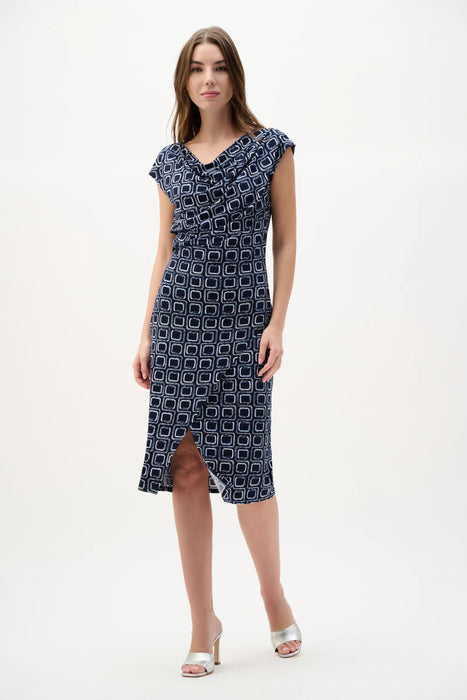 Woman wearing Joseph Ribkoff midnight blue multi geometric print sheath wrap dress with draped neckline, knee-length cut, and a flattering fitted silhouette.