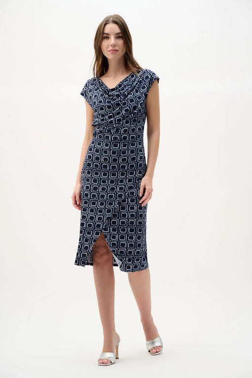 Woman wearing Joseph Ribkoff midnight blue multi geometric print sheath wrap dress with draped neckline, knee-length cut, and a flattering fitted silhouette.