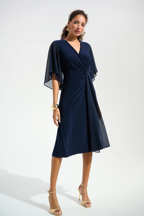 Woman wearing a navy blue knee-length dress with surplice neck and flutter chiffon sleeves from Joseph Ribkoff