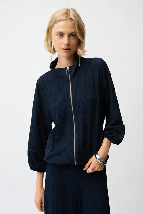 Woman wearing a navy blue zip front bomber jacket puff sleeves and mock neck from Joseph Ribkoff