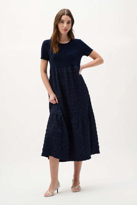 Woman wearing Joseph Ribkoff midnight blue trapeze dress with mixed fabric design styled for evening wear, events, and elegant modern occasions.