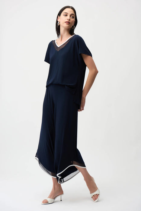 Woman wearing a dark blue one-piece wide jumpsuit with mesh insert and contrast trim at the v-neck and hem from Joseph Ribkoff