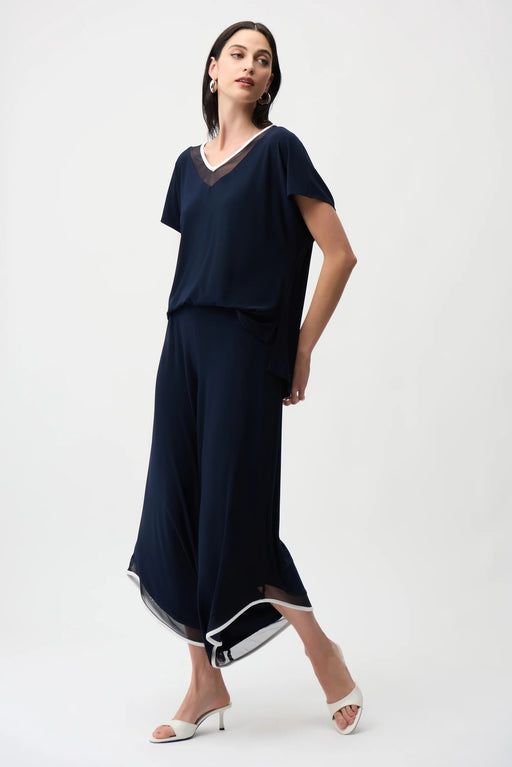 Woman wearing a dark blue one-piece wide jumpsuit with mesh insert and contrast trim at the v-neck and hem from Joseph Ribkoff