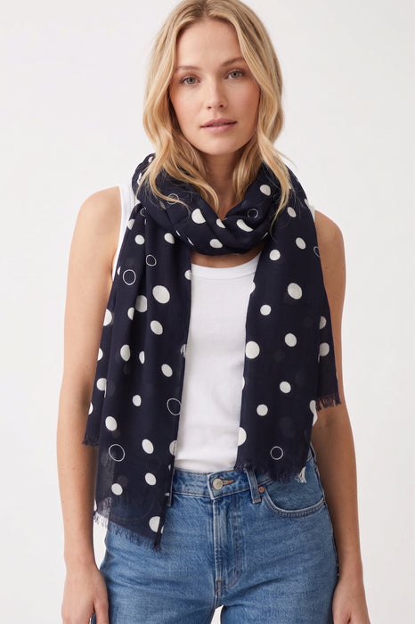 Woman wearing a navy blue scarf with white polka dots and fringe edges from Joseph Ribkoff