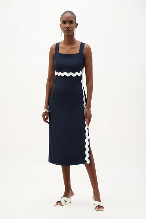 Woman wearing a navy blue sleeveless midi dress with white contrast trim, square neck, and side slit from Joseph Ribkoff