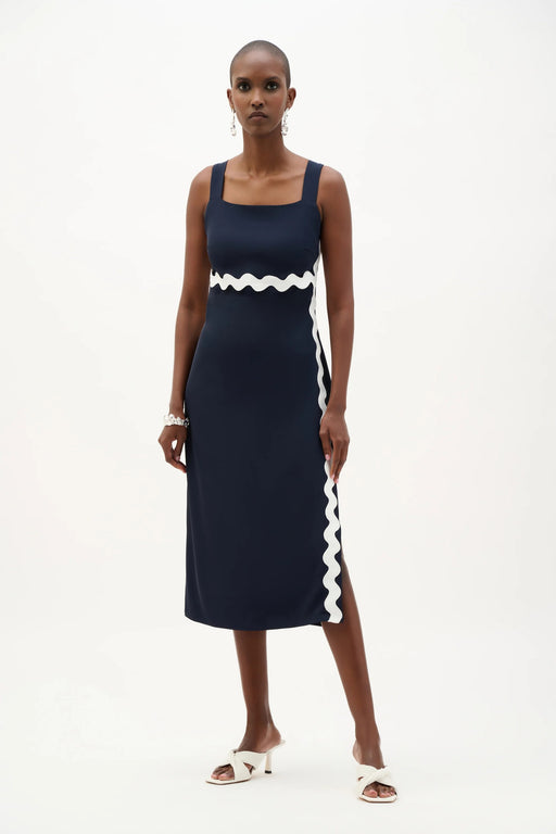 Woman wearing a navy blue sleeveless midi dress with white contrast trim, square neck, and side slit from Joseph Ribkoff