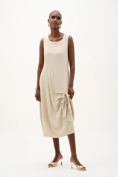 Woman wearing a moonstone textured cocoon dress with ring and tie detail, styled with gold heels for an elegant modern look