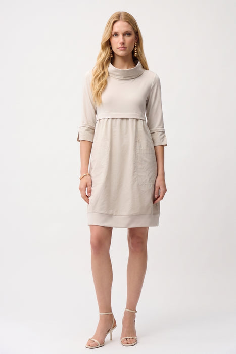 Woman wearing a knee-length cocoon dress with a cowl neckline, patch pockets, and fold-back cuff sleeves, styled for office wear, travel, or casual elegant occasions.