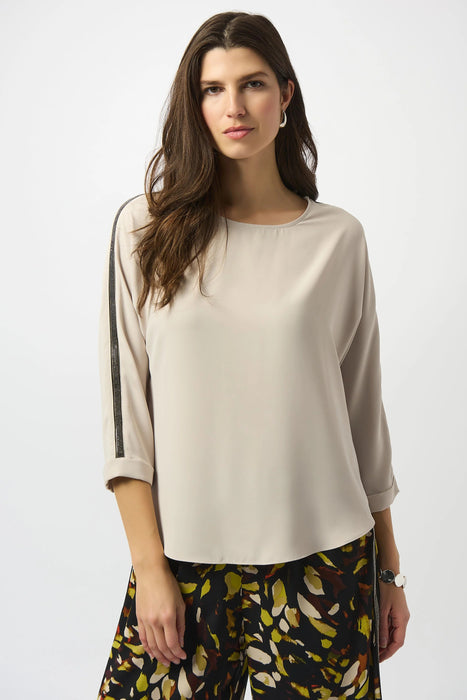 Woman wearing a beige lightweight blouse with contrasting rhinestone embellishments on the 3/4 sleeves