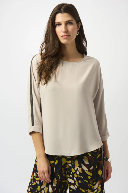 Woman wearing a beige lightweight blouse with contrasting rhinestone embellishments on the 3/4 sleeves