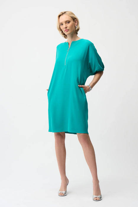 Woman wearing a turquoise shift dress with puff sleeves, zip front and side pockets from Joseph Ribkoff