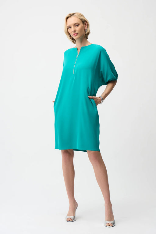 Woman wearing a turquoise shift dress with puff sleeves, zip front and side pockets from Joseph Ribkoff
