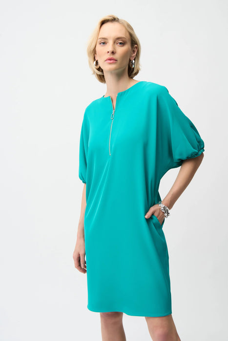 Woman wearing a turquoise shift dress with puff sleeves, zip front and side pockets from Joseph Ribkoff