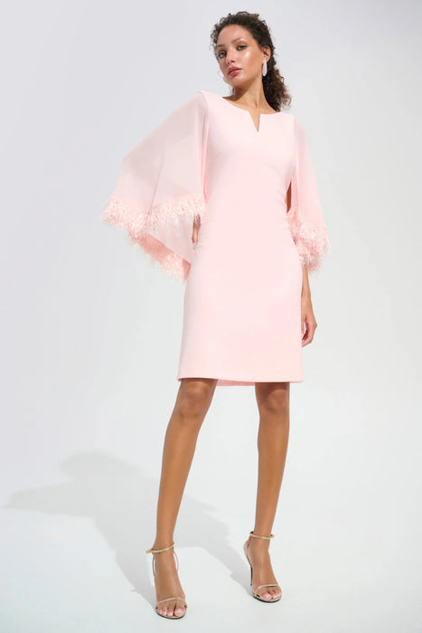 Woman wearing light pink A-line above the knee dress with sheer cape sleeves and slit neck from Joseph Ribkoff