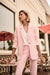 Woman wearing a light pink fitted blazer jacket with flap pockets and gold rose button from Joseph Ribkoff