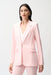 Woman wearing a light pink fitted blazer jacket with flap pockets and gold rose button from Joseph Ribkoff