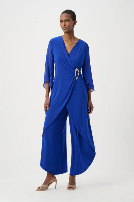 Woman wearing a blue wrap jumpsuit with 3/4 sleeves and cropped tulip wide leg from Joseph Ribkoff