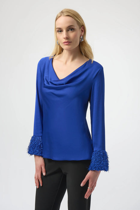Woman wearing a blue satin blouse with cowl neck and fringe cuffs