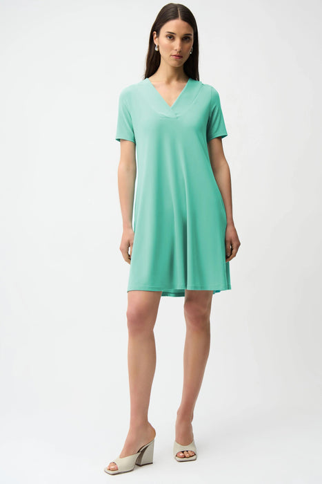 Woman wearing Joseph Ribkoff seafoam overlapping V-neckline A-line dress, featuring a soft flowy silhouette, short sleeves, and a flattering knee-length fit.