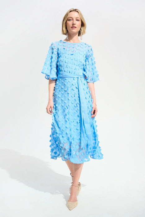 Woman wearing a light blue midi dress with 3D floral details and waist sash from Joseph Ribkoff