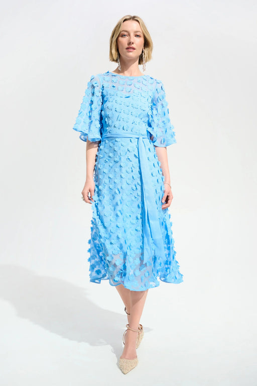 Woman wearing a light blue midi dress with 3D floral details and waist sash from Joseph Ribkoff