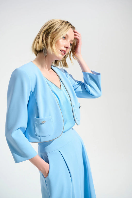 Woman wearing a light blue open front cropped jacket with rhinestone trim and front pockets from Joseph Ribkoff