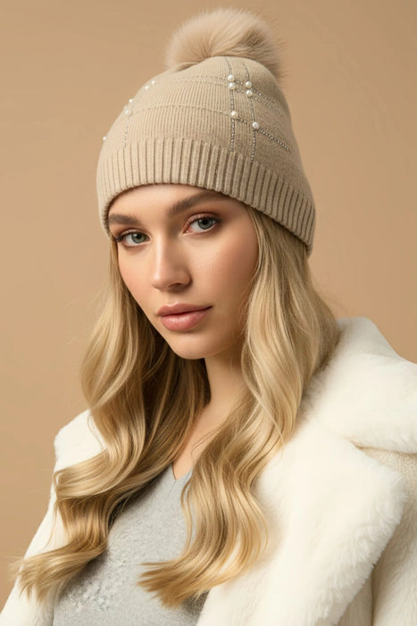 Woman wearing a beige knit beanie with a pom-pom and pearls from Joseph Ribkoff
