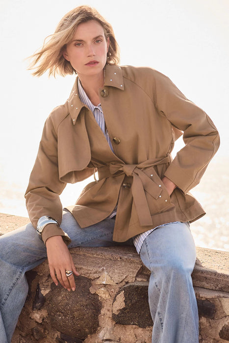 Woman wearing a tiger’s eye belted short trench coat with rhinestone details, styled with jeans and a striped shirt.