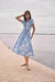 Woman wearing a Joseph Ribkoff vanilla and blue floral print fit and flare midi dress with short sleeves and a tie waist, styled for a chic summer look
