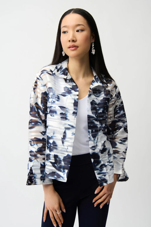 Woman wearing a vanilla and midnight blue floral trapeze jacket with stand collar and open front, styled over a white top and dark pants.
