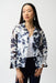Woman wearing a vanilla and midnight blue floral trapeze jacket with stand collar and open front, styled over a white top and dark pants.