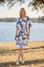 A woman wearing a short-sleeve white wrap-style dress with an abstract blue and gray stripe prints from Joseph Ribkoff