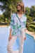 Woman wearing Joseph Ribkoff cotton stripe floral print boxy blouse, featuring lightweight breathable fabric, relaxed fit, bold green floral design, and chic casual styling paired with white pants.