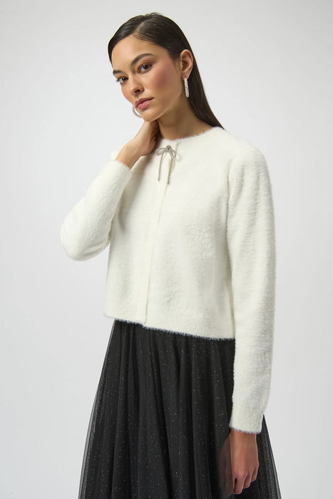 Woman wearing a white feather yarn knit cardigan with rhinestone bow detail from Joseph Ribkoff