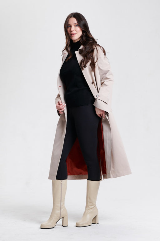 A woman modeling a long beige trench coat with button front closure and self-tie belt from Nikki Jones