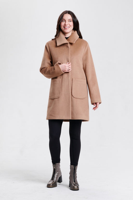 A woman modeling a camel brown mid-length coat with a wide collar, front button closure, and large patch pockets from Nikki Jones